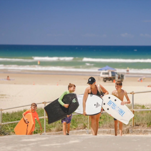 A family walking up the ramp from the beach with boogie boards