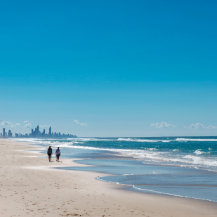 Two people in the distance walking on a Gold Coast beach by the water on a sunny day