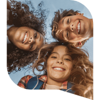 Three kids grin down at the camera from above with their heads together.