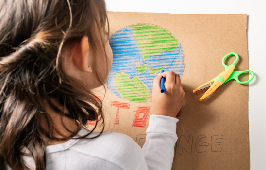 A young girl is colouring in a picture of the earth on brown paper
