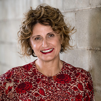 Professional head shot of yourtown CEO Tracey Adams in a floral red top smiling with red lipstick 